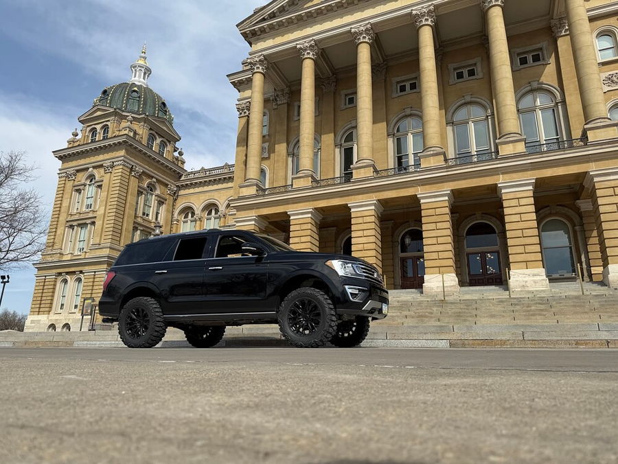 Side profile lifted Troy's black 2018 Ford Expedition with large off-road tires before ornate classical yellow stone building gallery photo 3