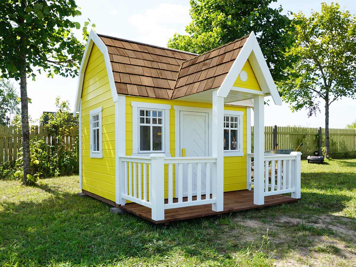 Wooden Playhouse in yellow color with a white terrace in a sunny garden by WholeWoodPlayhouses