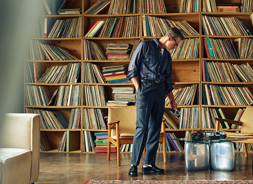 Person standing near a large collection of vinyl records in a cozy room.