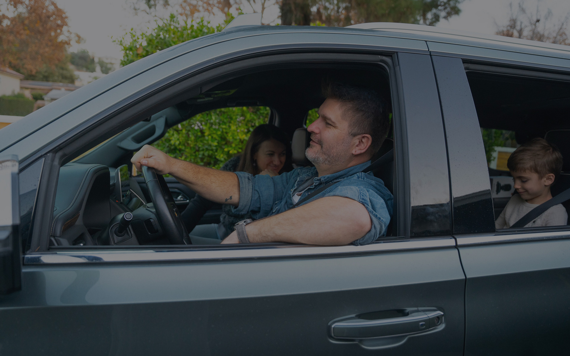 Man driving a car with two passengers inside.