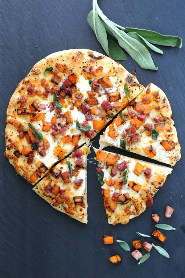 Baked pizza topped with cheese, cubed butternut squash and pancetta and sliced for serving
