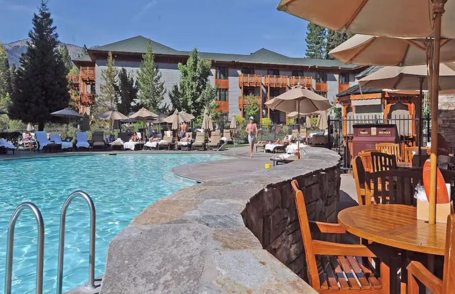 Hotel poolside with lounge chairs, tables, and umbrellas under a clear blue sky.