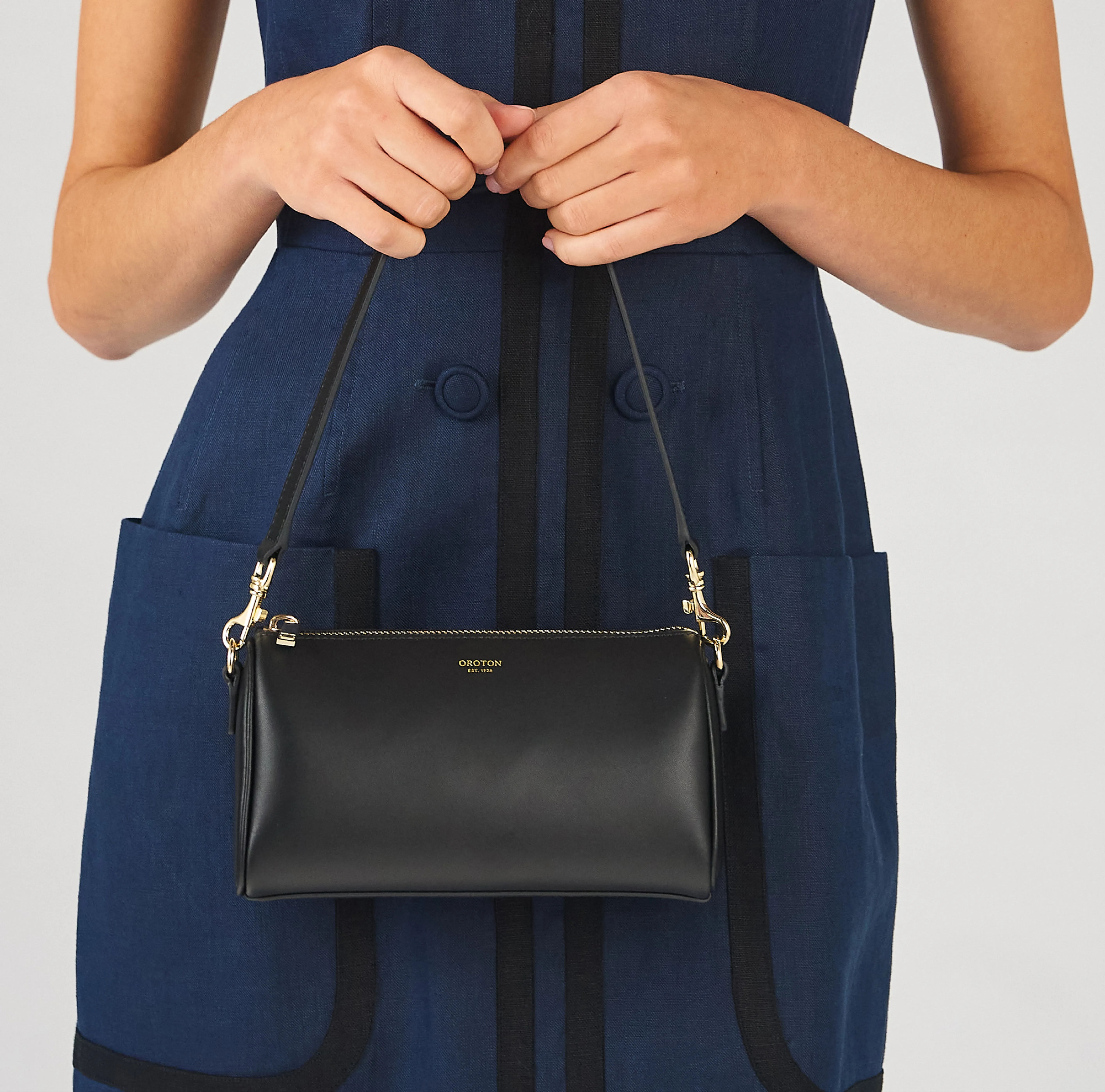 A person holding a small black handbag while wearing a blue dress.