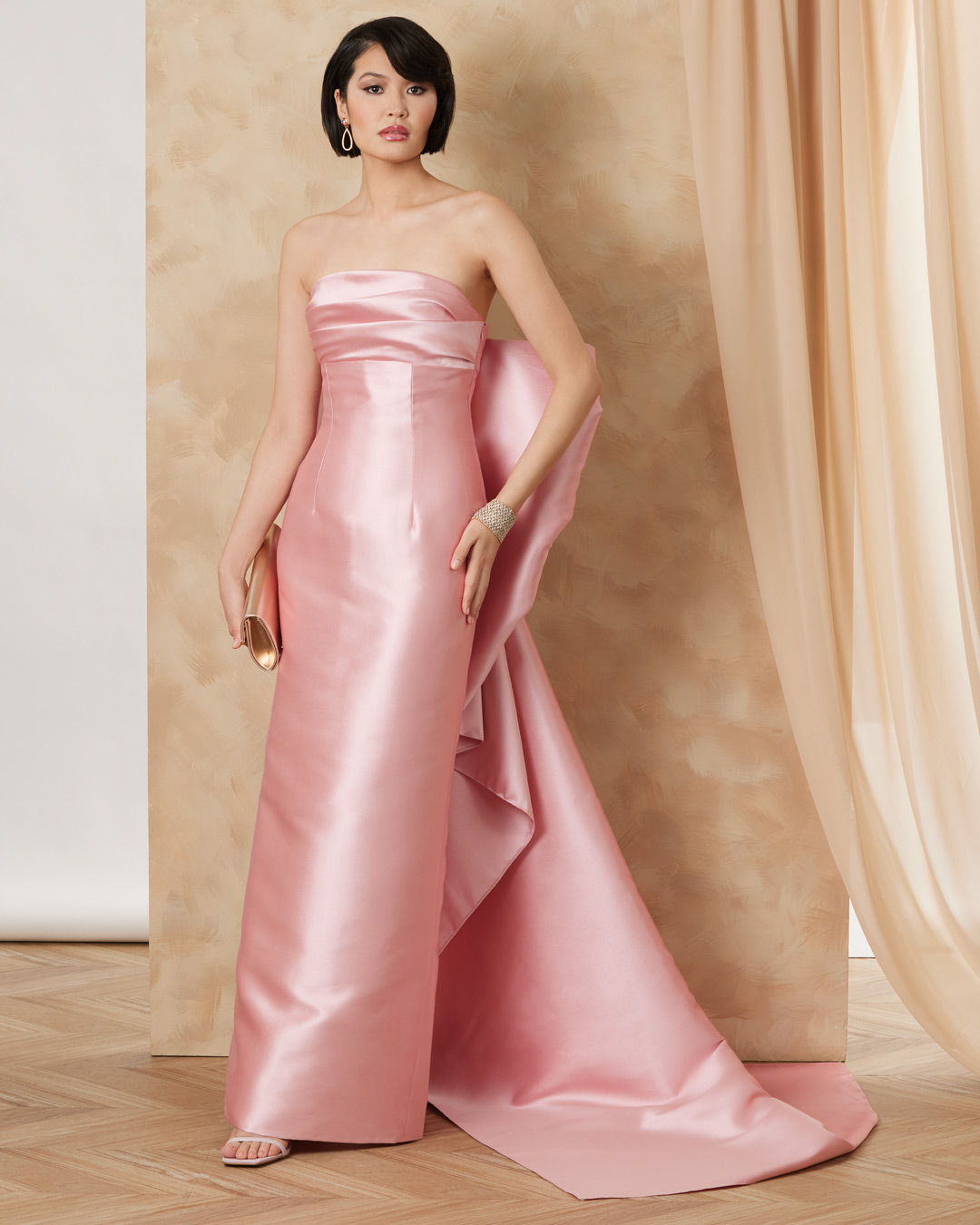 A woman wearing a strapless pink gown standing against a neutral backdrop.