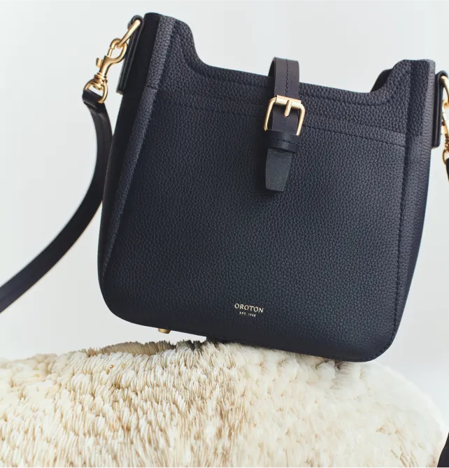 Black handbag with a shoulder strap resting on a beige surface.