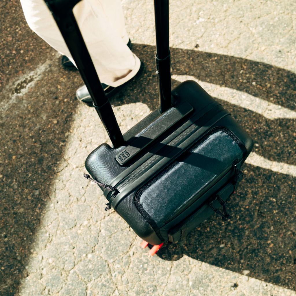 A black wheeled suitcase on a textured surface with a person's leg nearby.