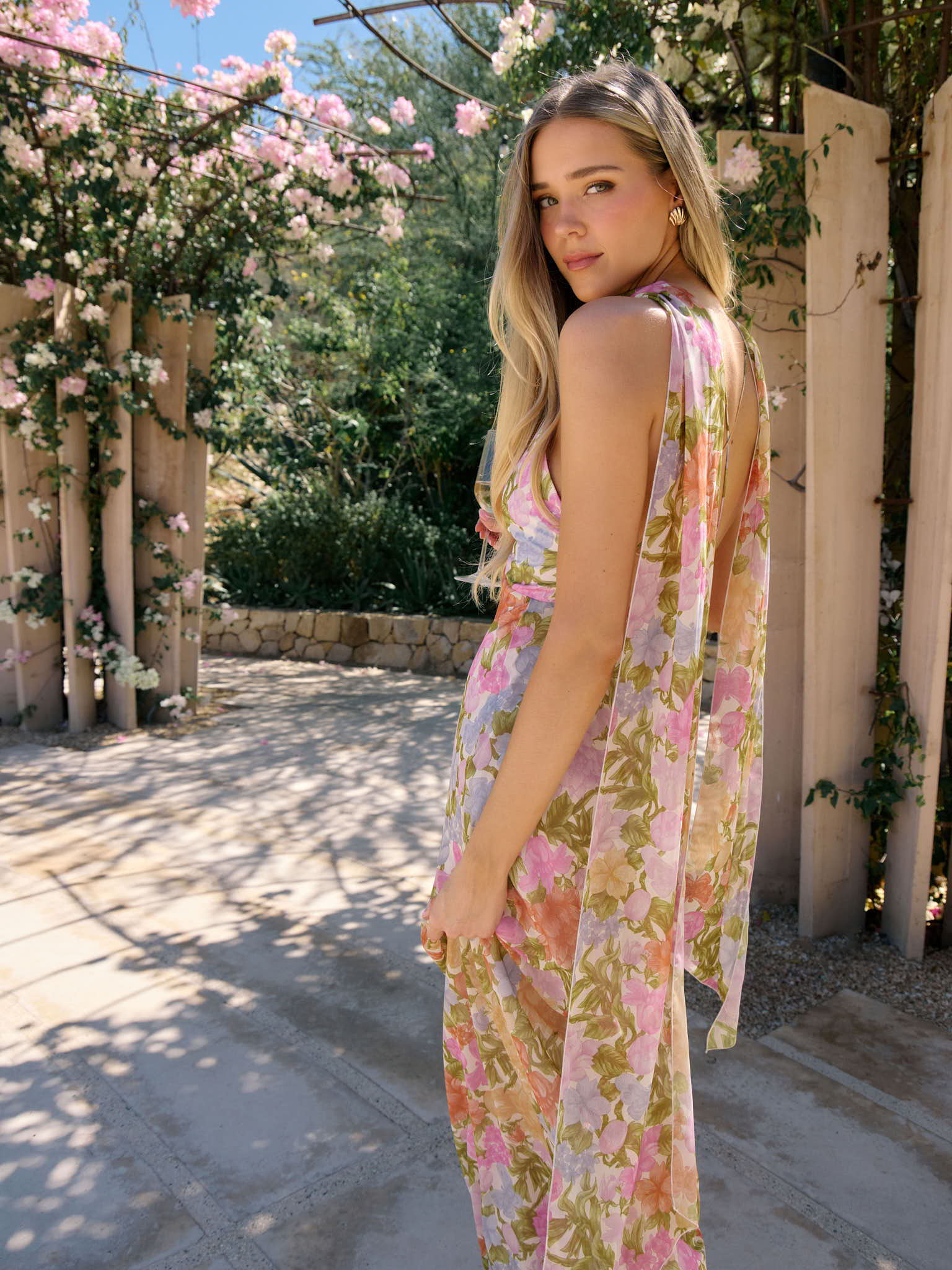 Person in a floral dress standing in a garden pathway with blooming flowers.