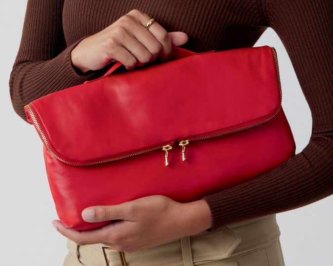 Person holding a red handbag with a zipper closure.