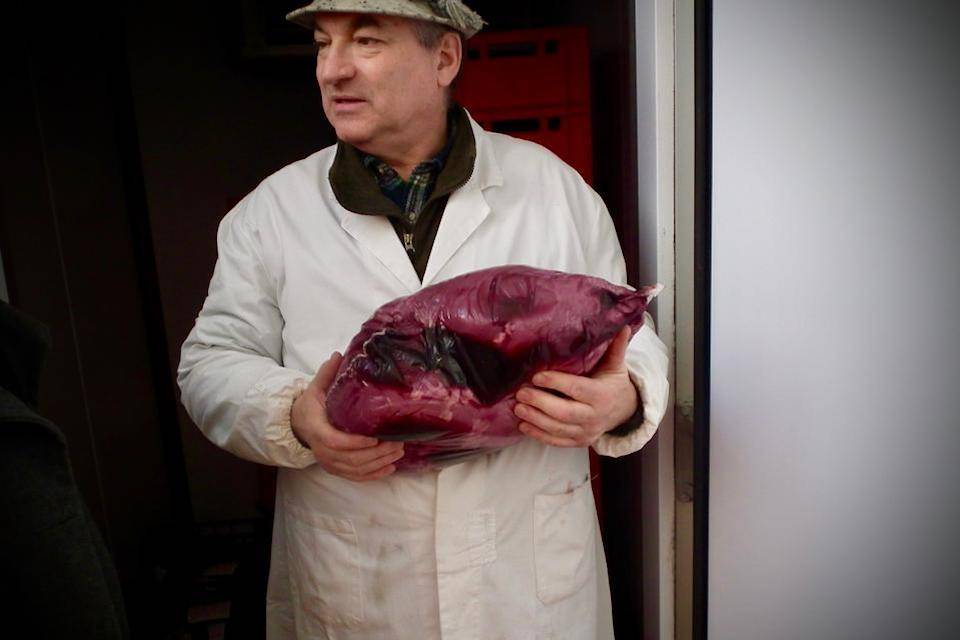 An artisan producer stands in butchers' whites holding a large Italian bresaola