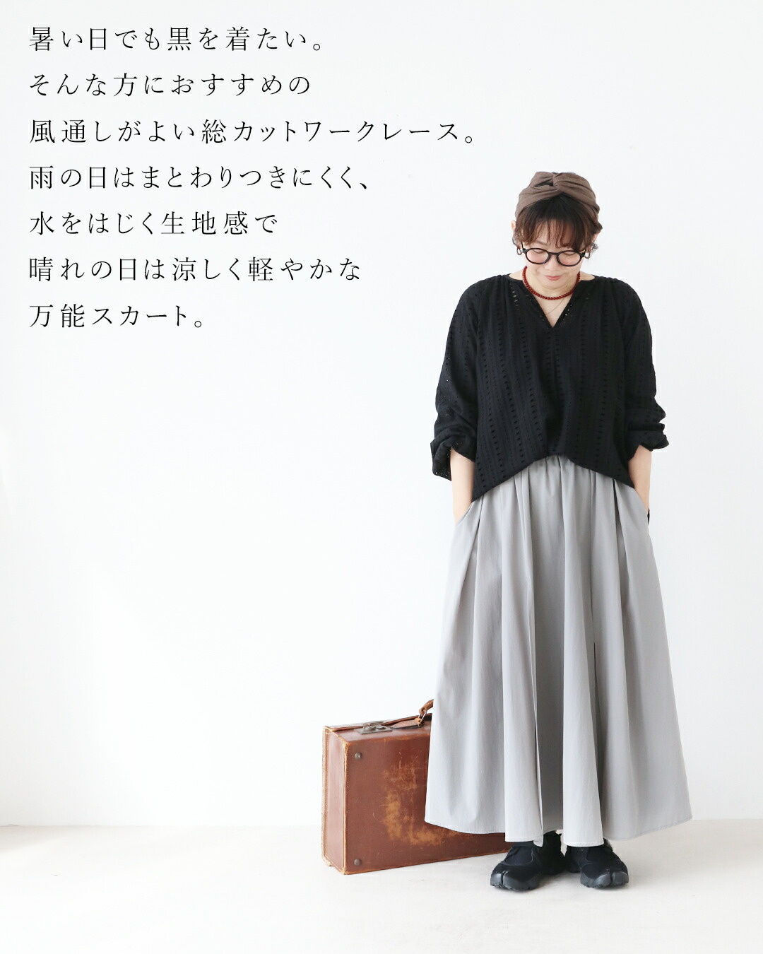 Woman in a black top and gray skirt, standing with a bag.