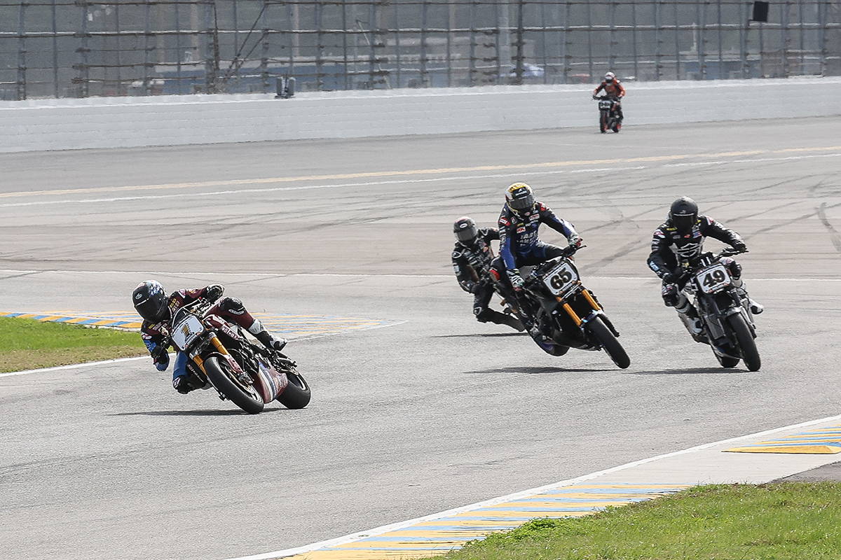 Tense moment as multiple racers in a mix of vibrant racing suits aggressively corner on the Daytona track, demonstrating skill and high-speed maneuvering in close quarters.
