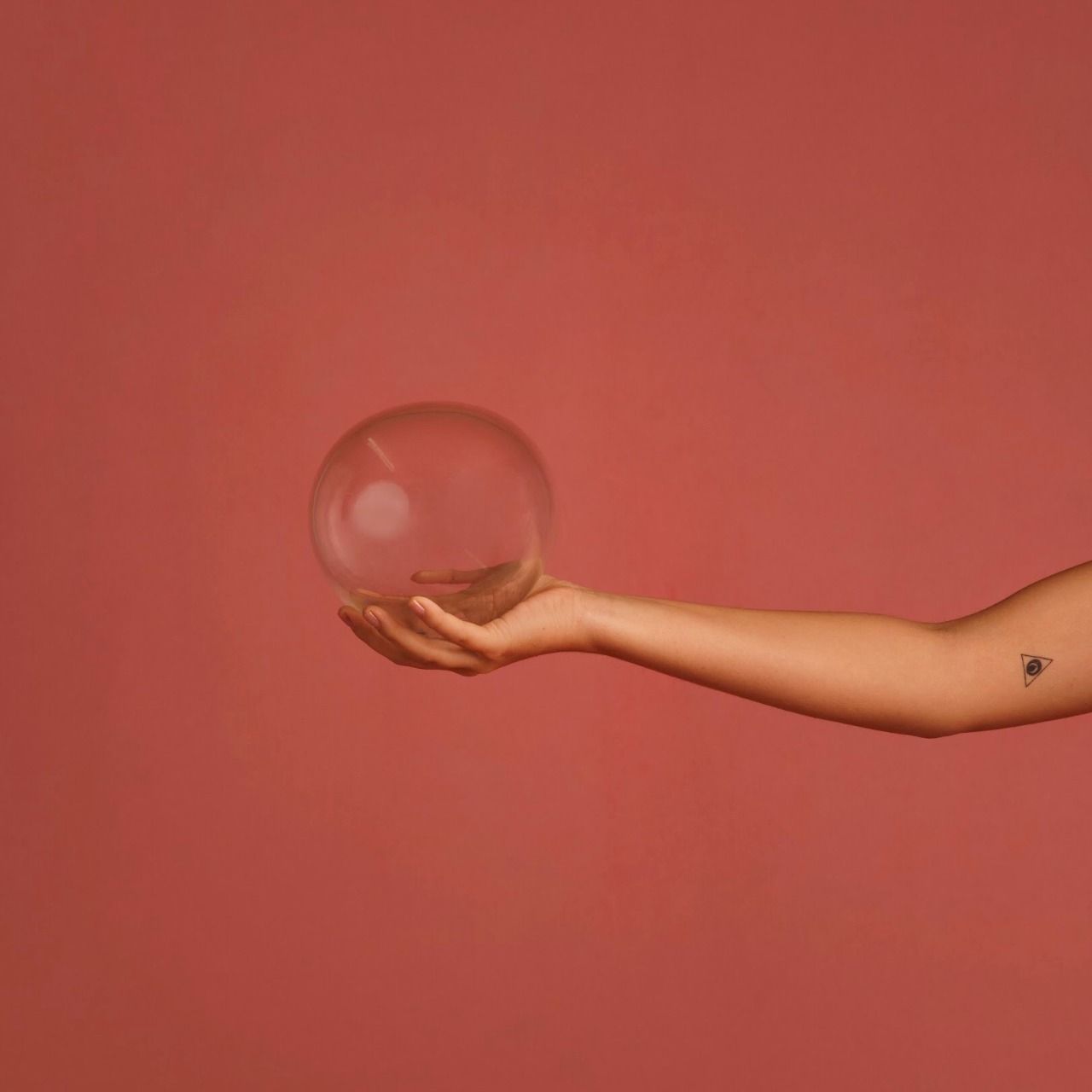 Braço feminino contento uma pequena tatuagem segurando um globo de vidro
