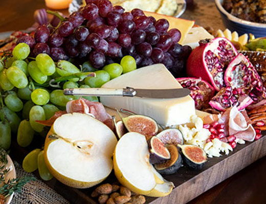 A wooden platter with various fruits, cheese, and nuts arranged beautifully.