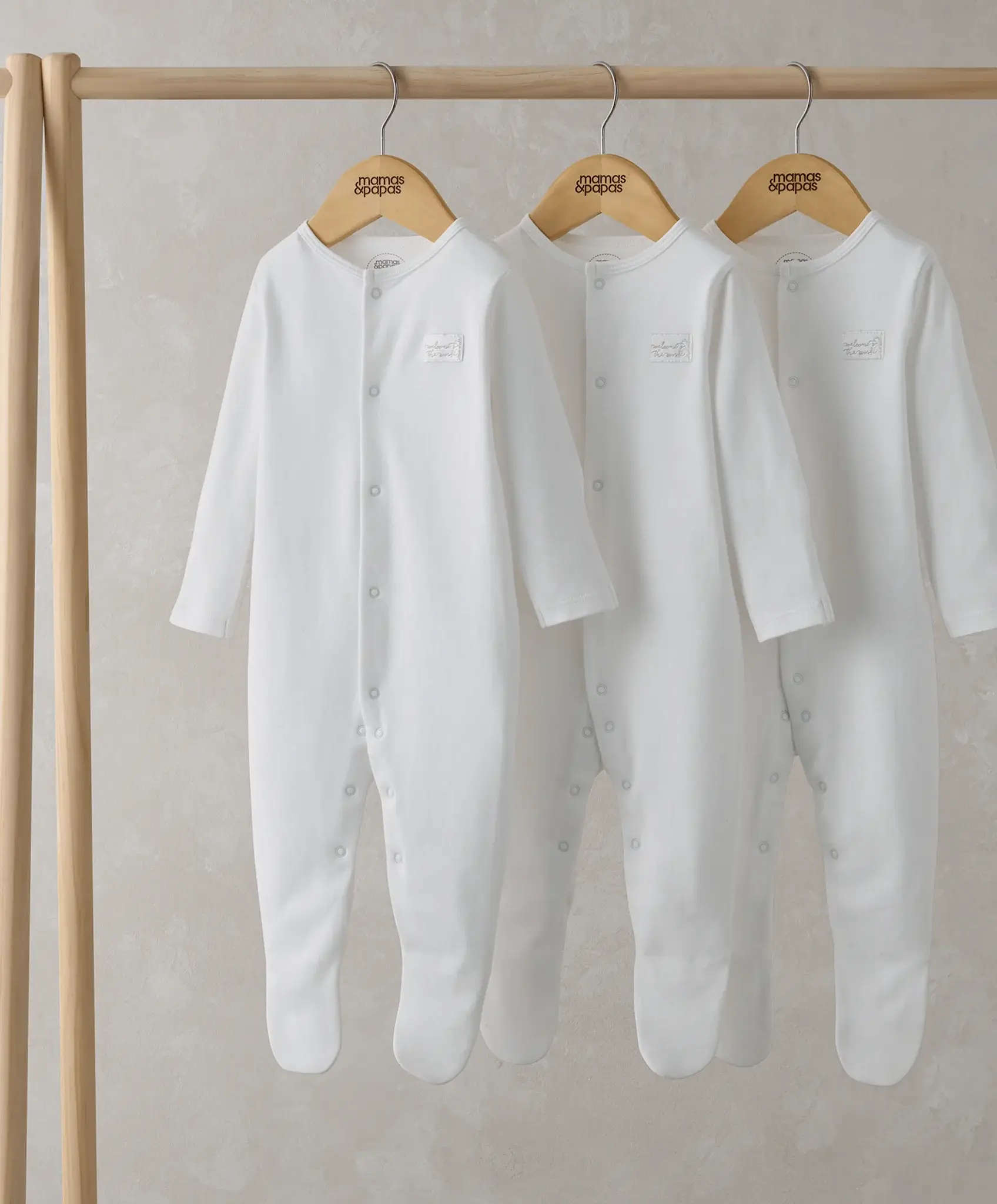 Three white infant rompers hanging on wooden hangers.