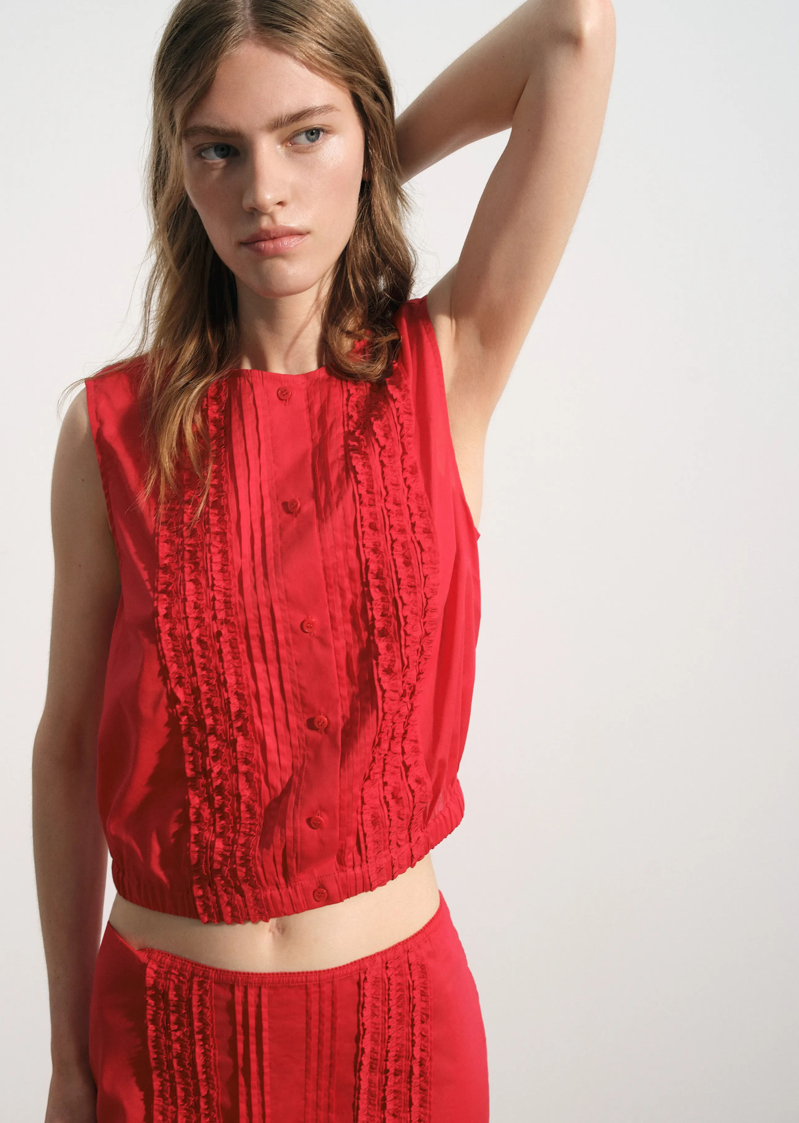 Model wearing a red sleeveless top with textured details.