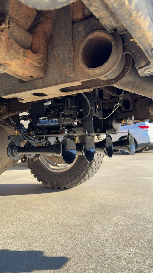 Low-angle under rear spare tire well view Conductor's Special 2HB Shocker XL train horns air tank and HornBlasters air compressor mounted on Craig's 2016 Chevy Silverado 2500HD frame and suspension gallery photo 2