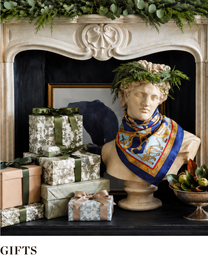 Decorative gifts arranged around a bust with greenery and a scarf.