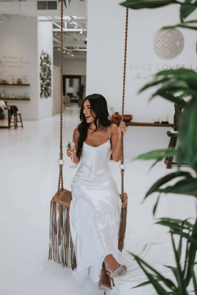 Mariée portant une robe en soie à fines bretelles sur une balançoire doublée de cuir à l'intérieur d'une salle d'exposition nuptiale.