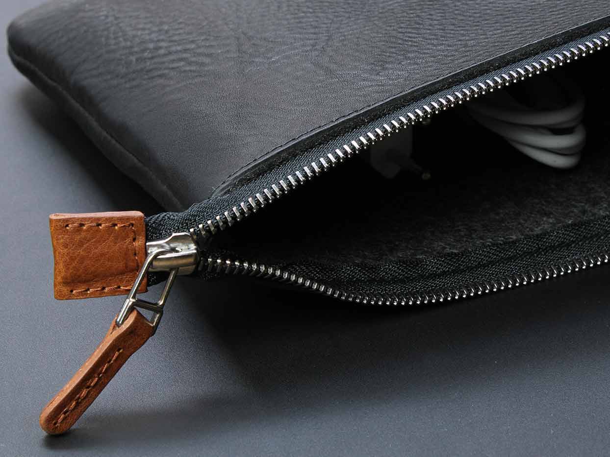 Auf einem Tisch liegt eine offene Tasche aus Leder in Schwarz mit Cognac farbenen Detail am Reißverschluss