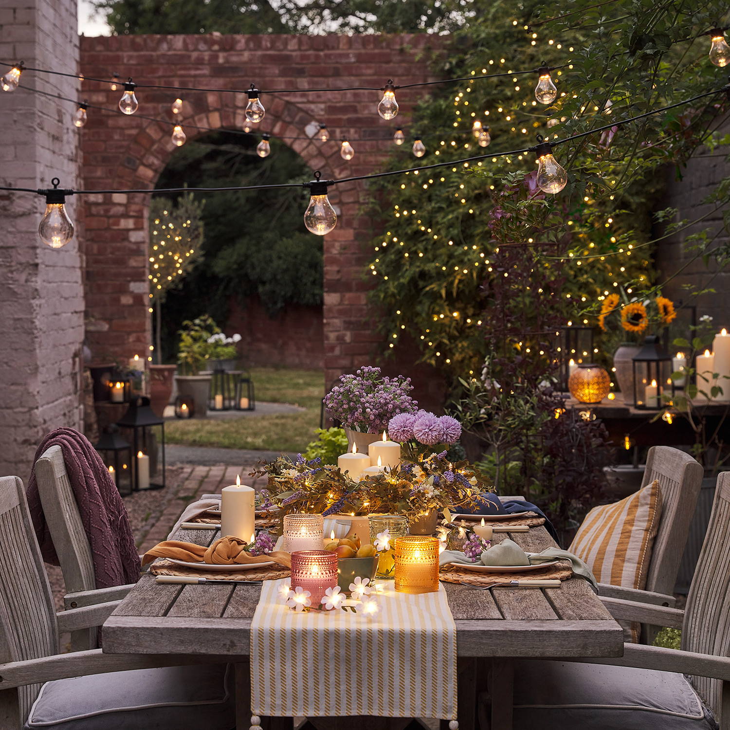 An alfresco summer dining setting with LED candles, festoon lights and fairy lights in the backdrop.