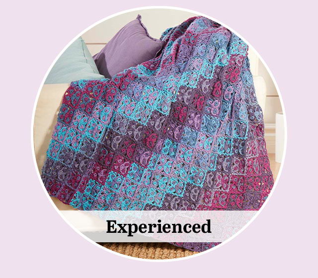 Colorful patterned blanket draped on a surface with pillows. Text 