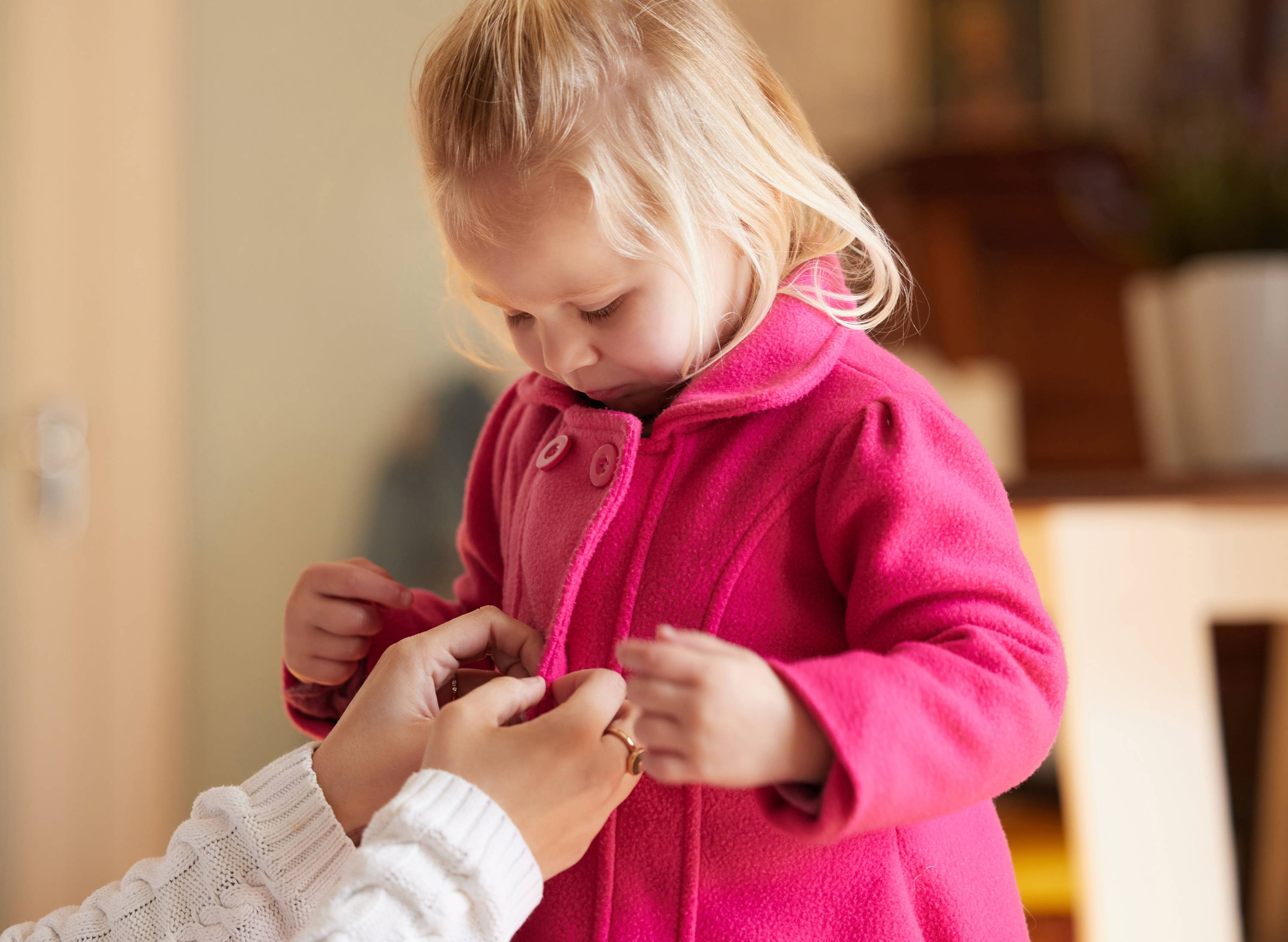 mom putting coat on little girl