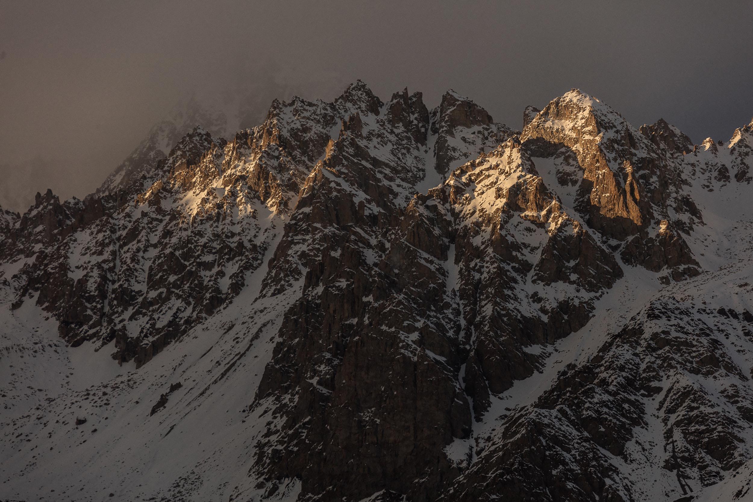 Snowy mountain peaks illuminated by soft light under a cloudy sky.