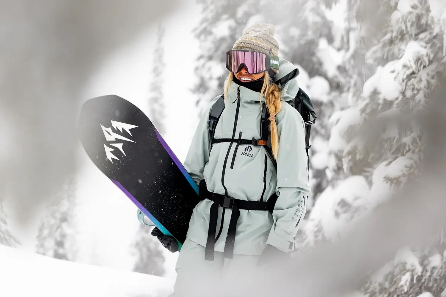 Snowboarder in winter attire standing in snowy landscape, holding a snowboard.