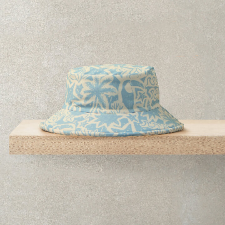 Light blue bucket hat with palm tree patterns on a wooden shelf.