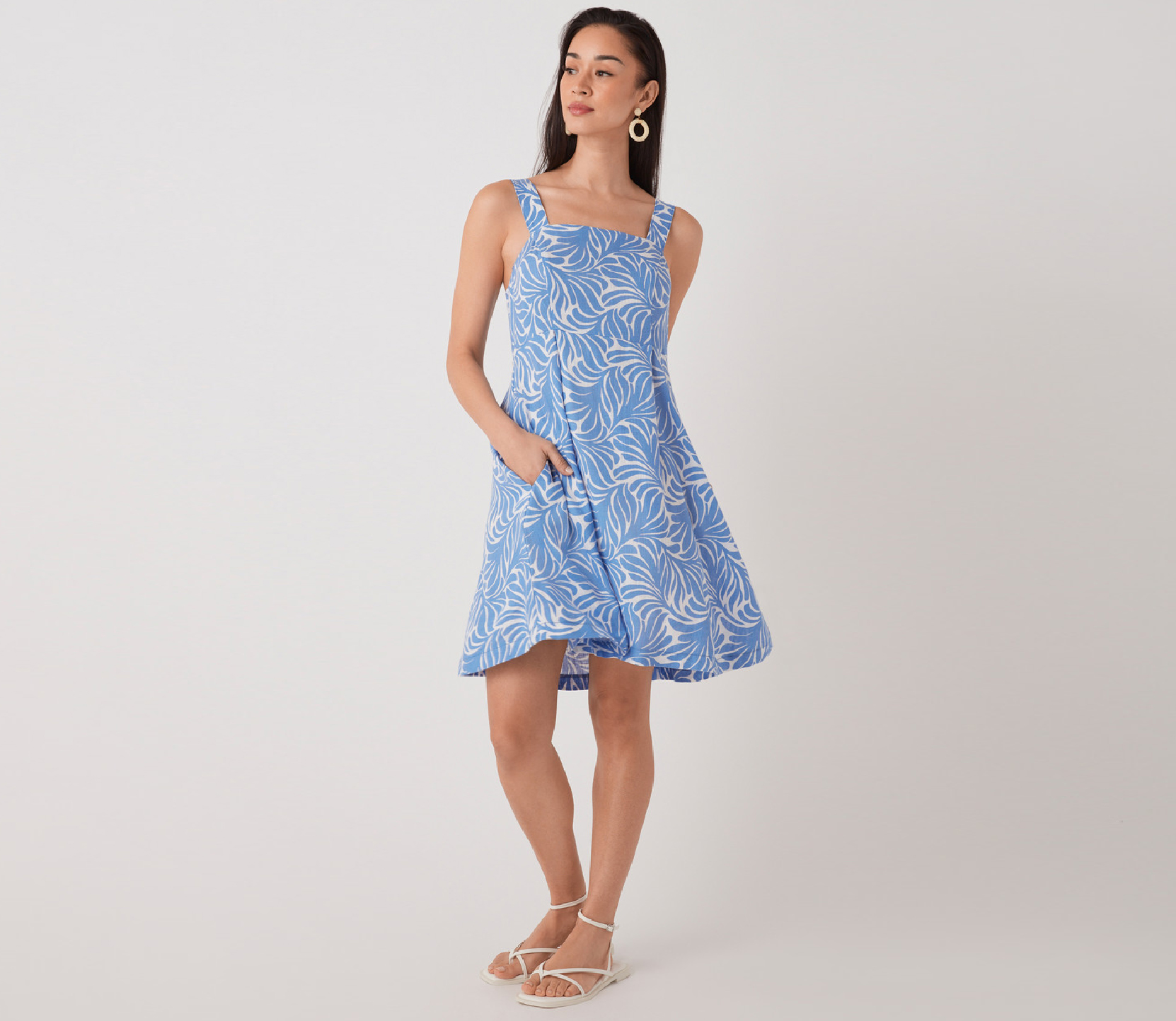 Woman in a blue floral dress with pockets, standing against a plain background.