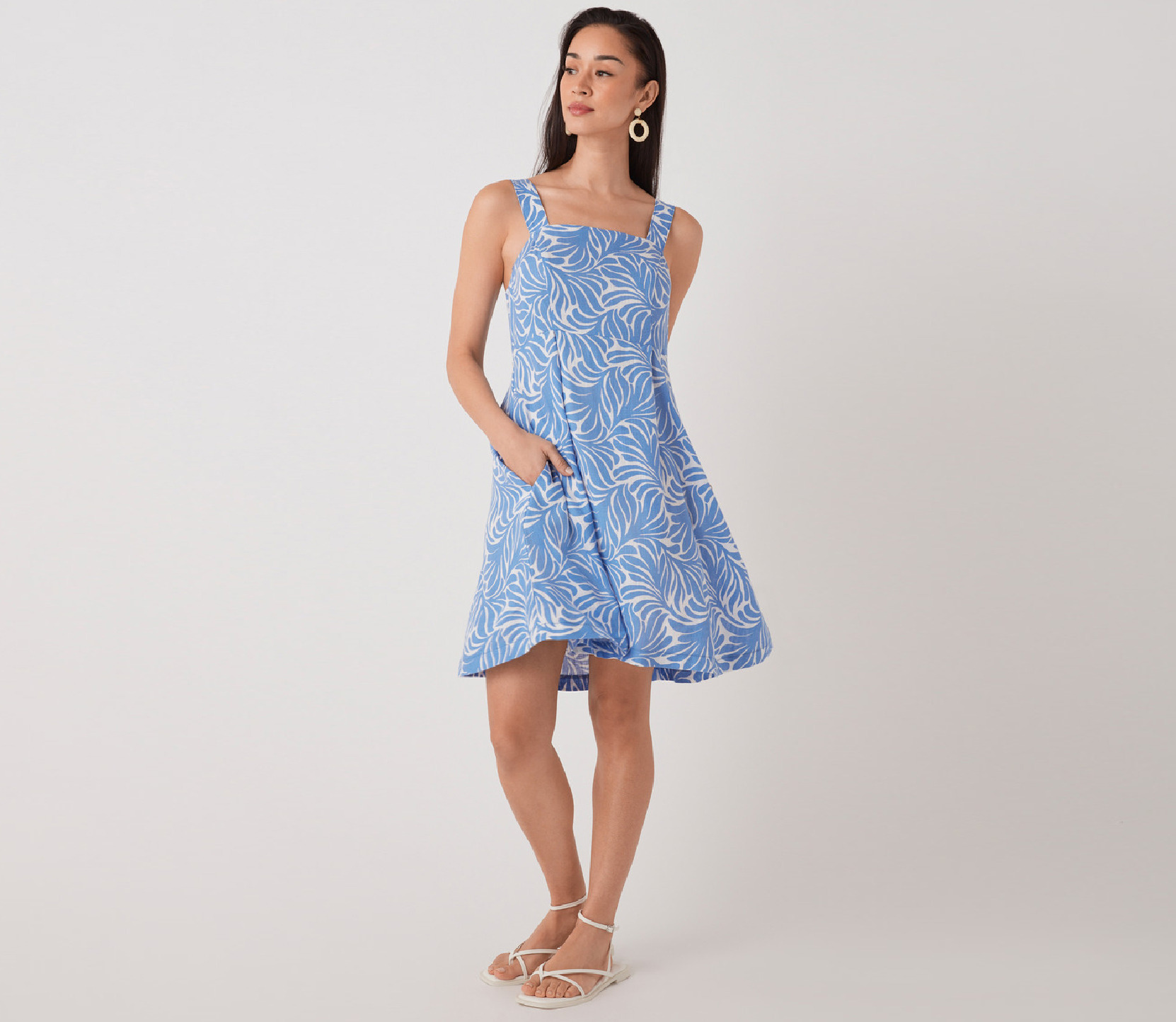 Woman in a blue floral dress with pockets, standing against a plain background.