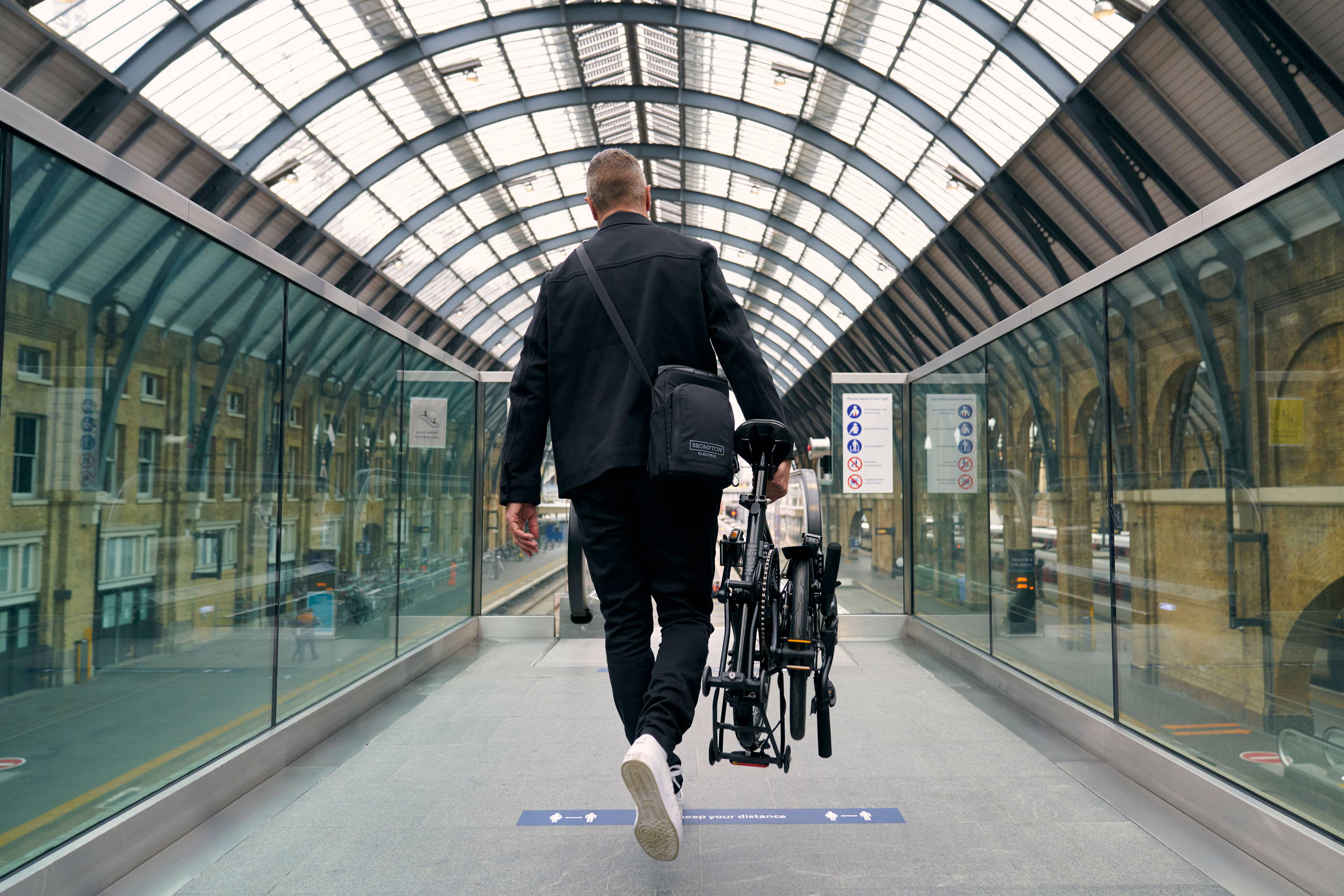 A man walks carrying a Brompton Electric P Line bike through a train station