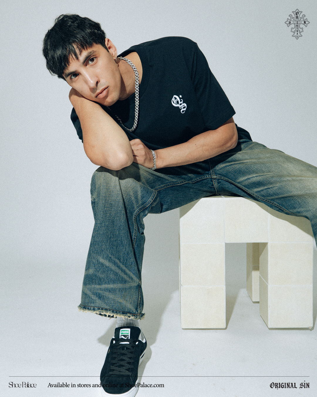 Young man sitting on a block, wearing a black t-shirt and jeans.