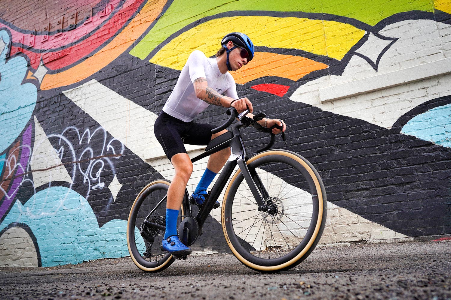 Cyclist riding a black Cervelo Aspero-5 in front of a colorful wall.