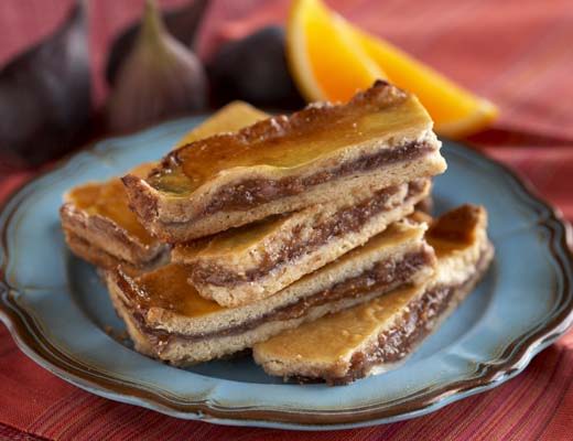 Stack of layered fig bars on a blue plate with figs and orange.