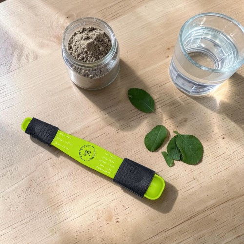 A green tool, jar of powder, leaves, and a glass of water on a table.