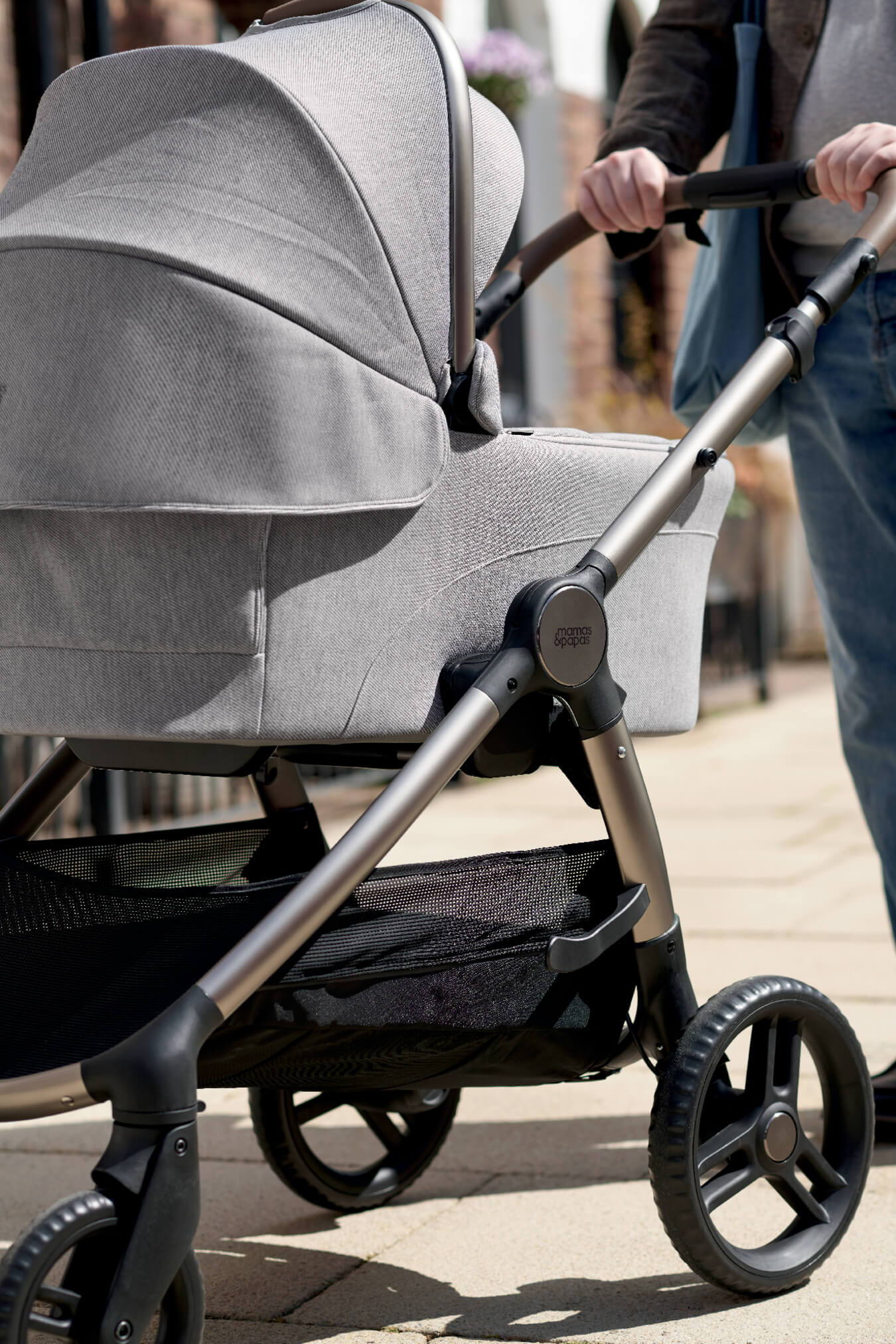 A person pushing an Ocarro 2 Heritage stroller on a sunny sidewalk.