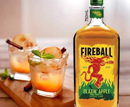 Bottle of Fireball Blazin' Apple with cocktails in glasses.