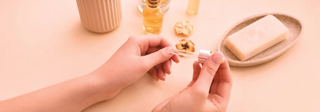 Hands holding a small container with essential oils, surrounded by beauty products.
