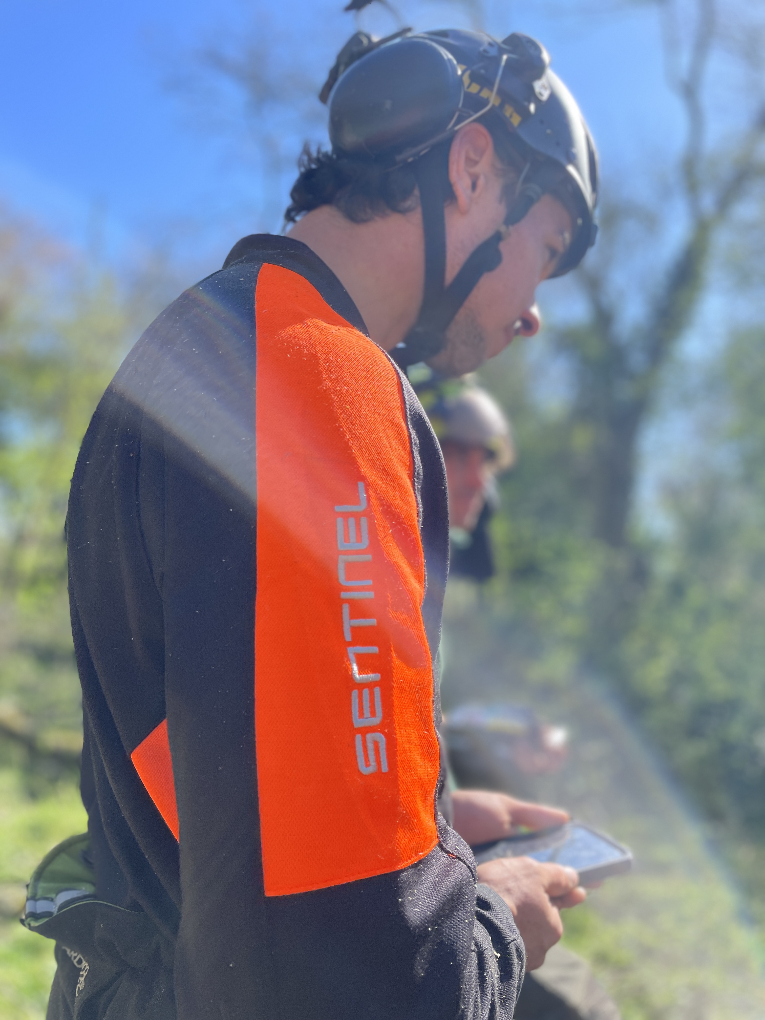 A person in a helmet using a phone outdoors, wearing a black and orange outfit.