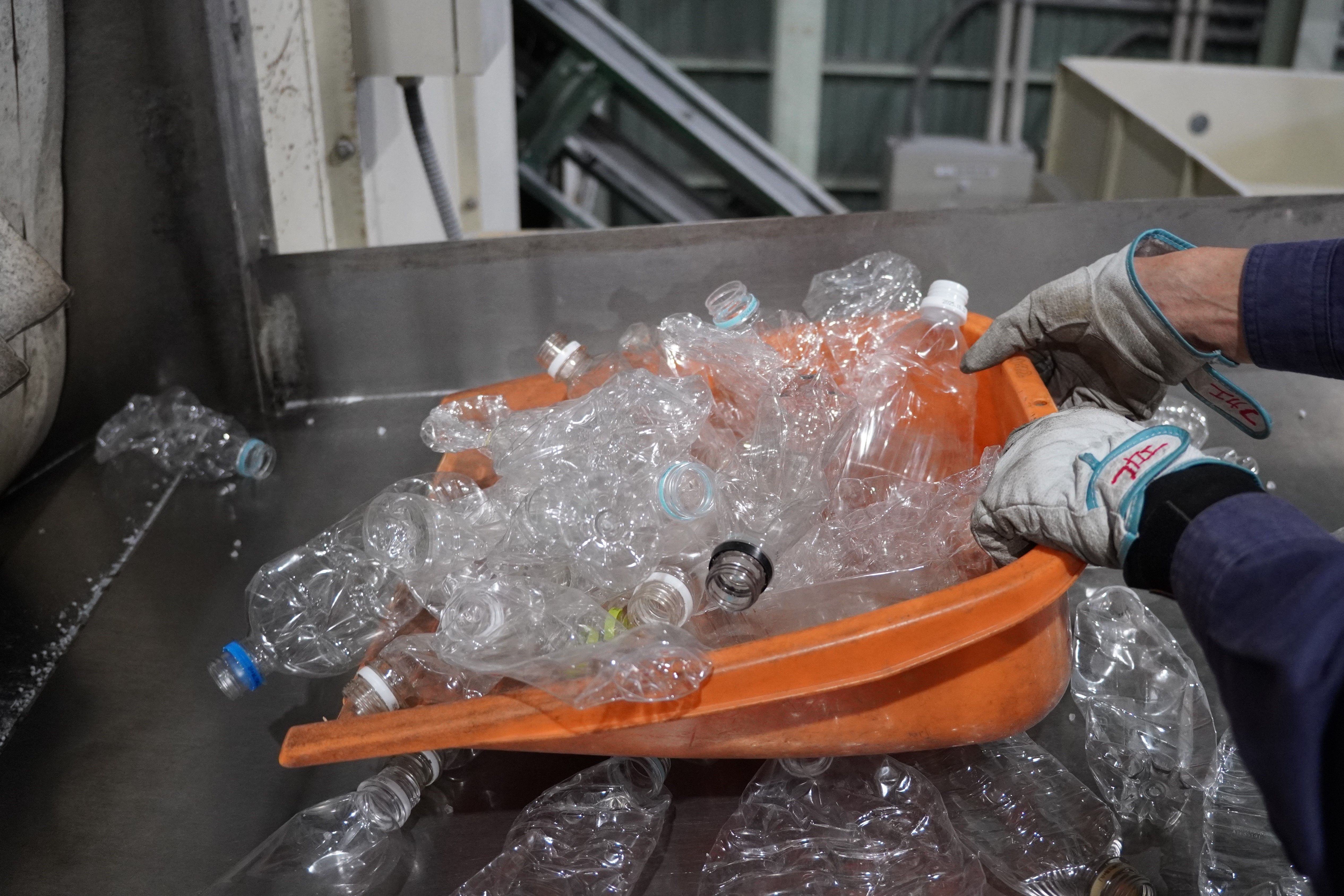 Person wearing gloves holding a wheelbarrow filled with plastic bottles.