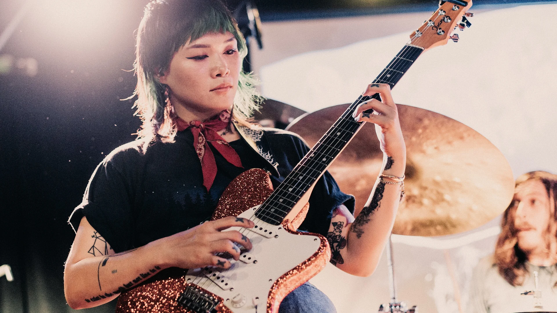Yvette Young playing guitar on stage with a drummer in the background.