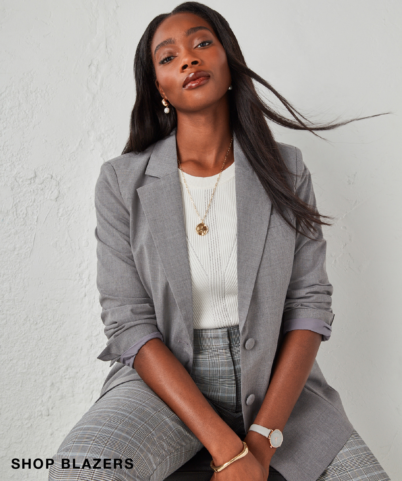 Woman in a gray blazer with long hair, posing confidently against a light background.