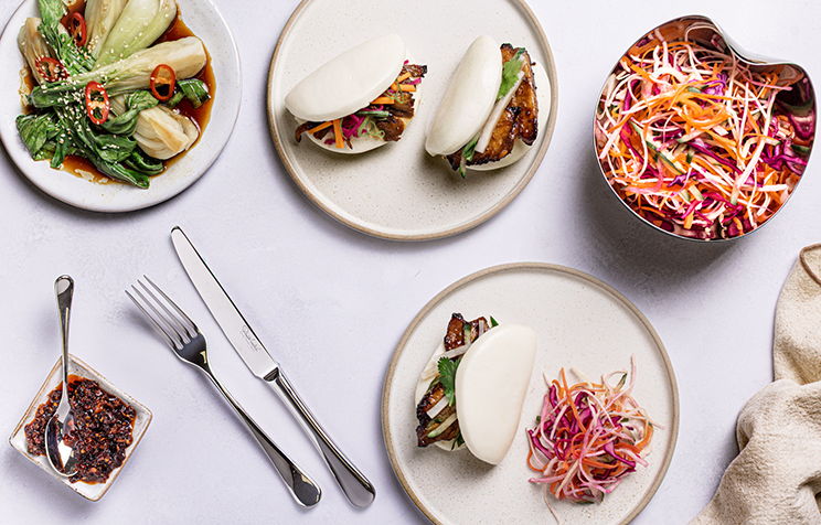 Plates of food including pork belly bao buns, salad, and a side dish.