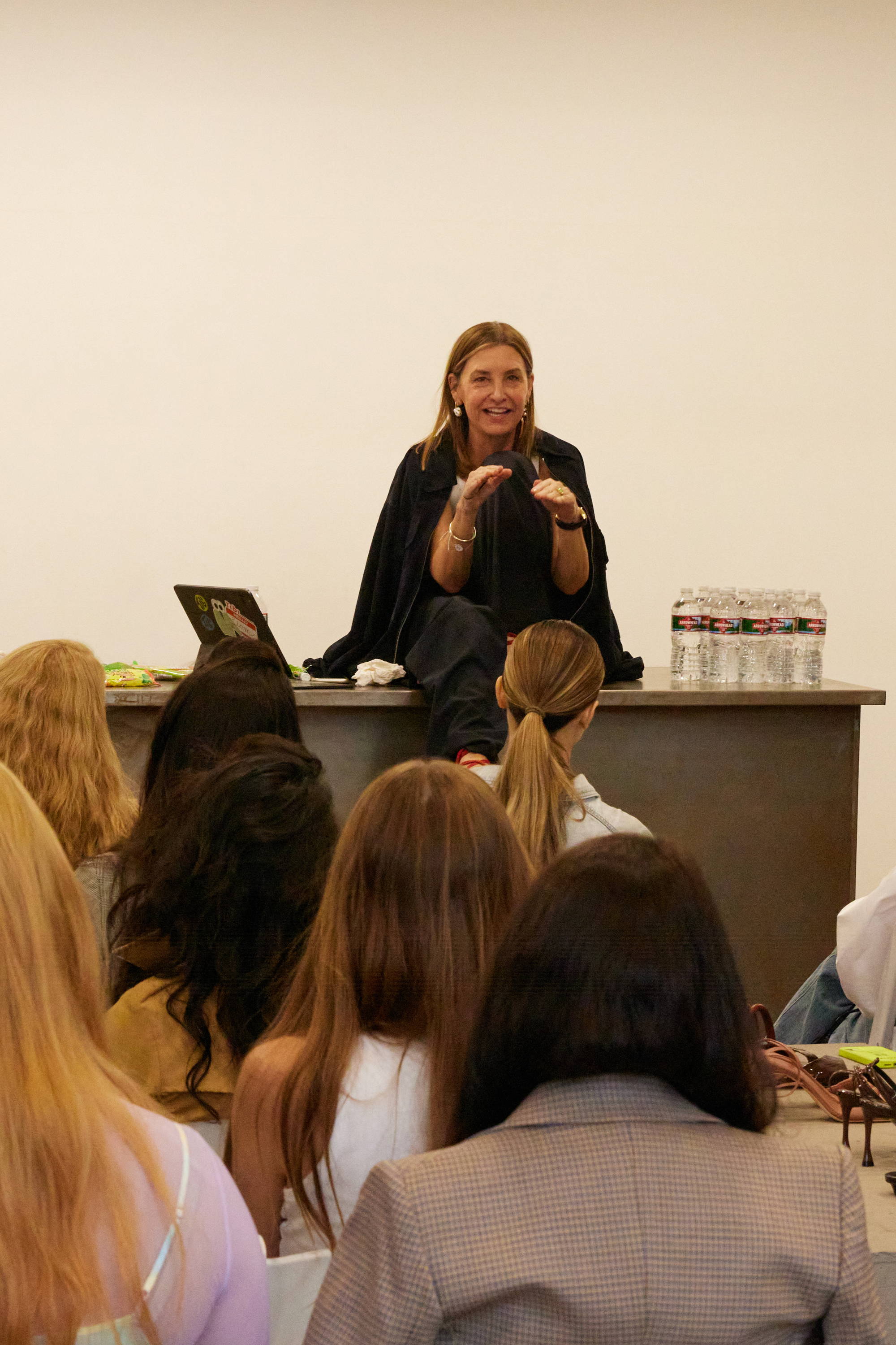 Woman sitting on a table speaking to an audience in a classroom setting.