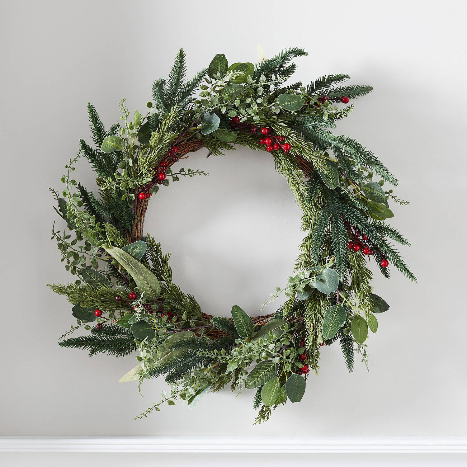 Pine and red berry wreath hung on wall
