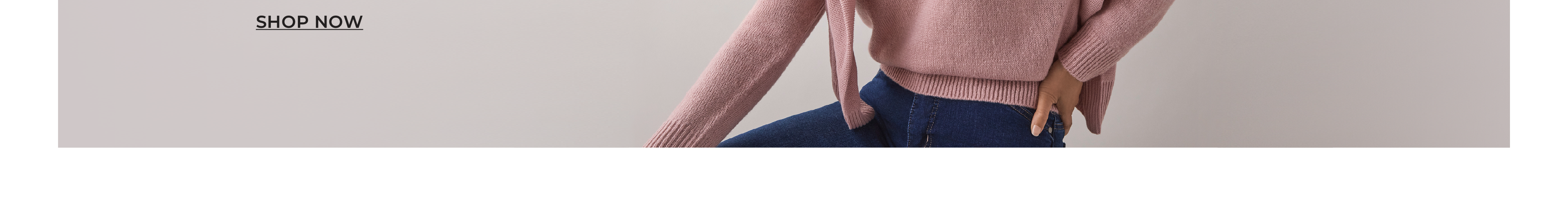 Model wearing a pink sweater and blue jeans, posing against a neutral background.