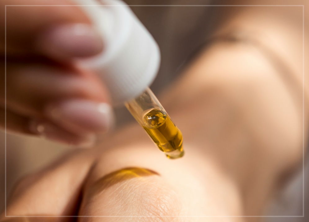 A pipette containing essential oil, being applied to someone's hand