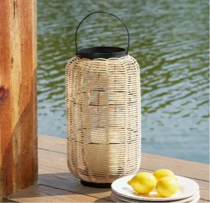 A wooden lantern sits on a ledge overlooking a lake. In front of the lantern is three lemons sitting on s stack of three plates.