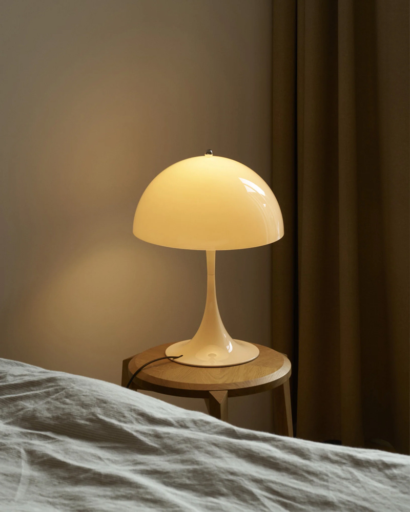 A modern Panthella Table lamp by Louis Poulsen on a wooden table beside a bed.